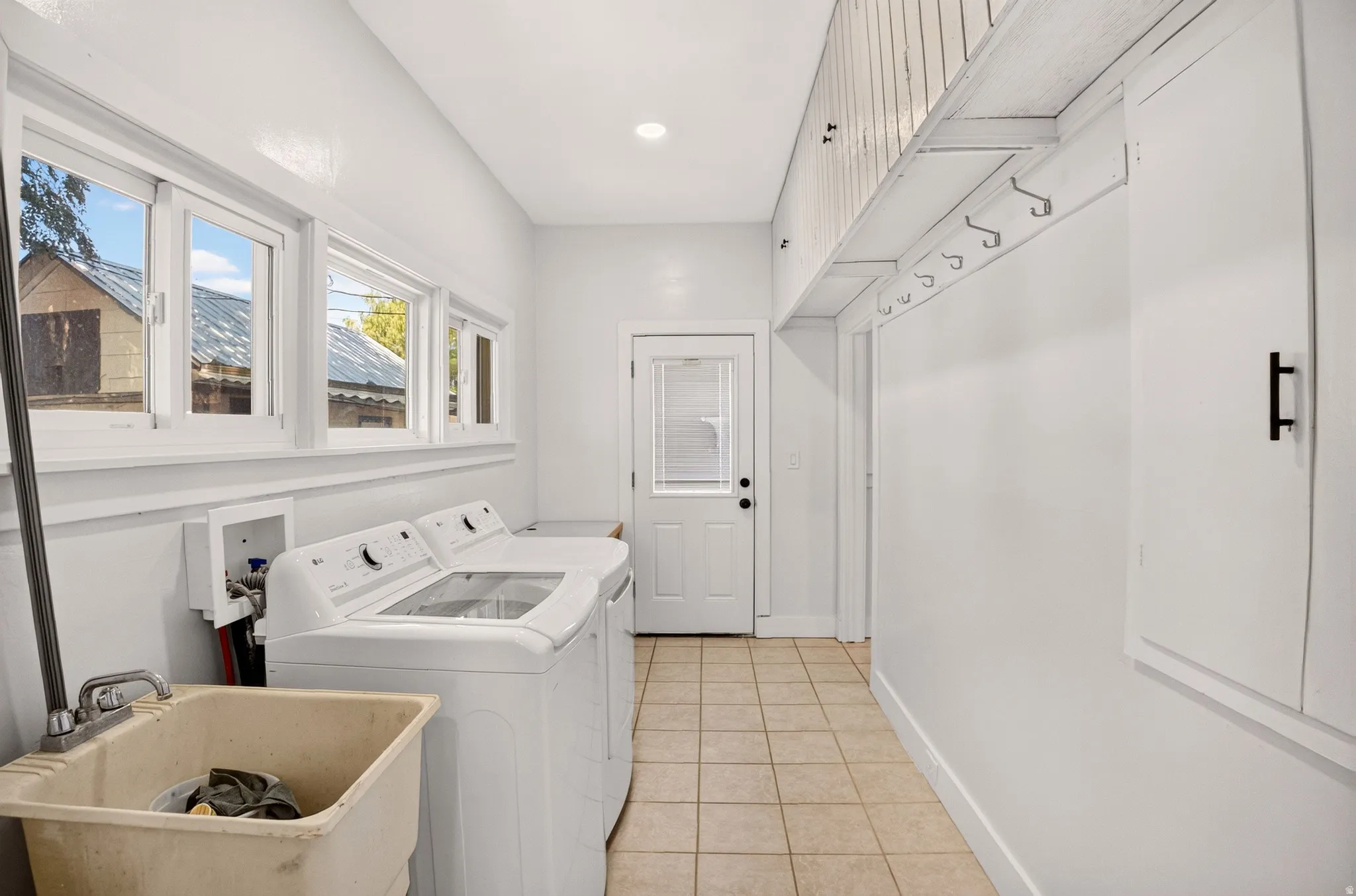 Utility room featuring ceramic tile flooring, a utility sink, and multiple windows