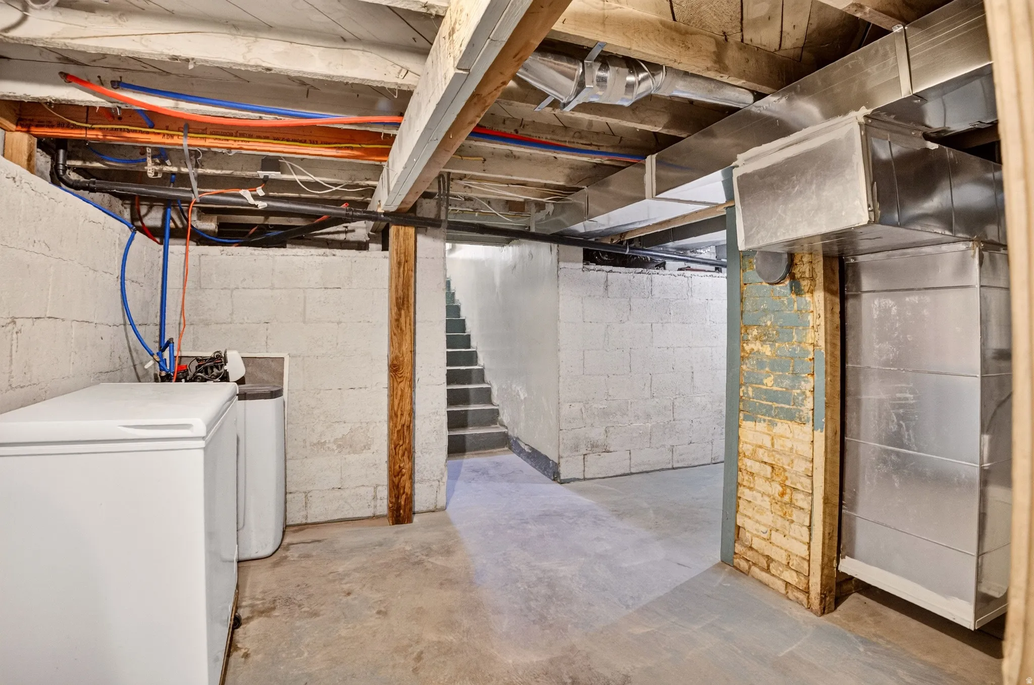 Basement space featuring exposed ceiling joists, concrete block walls, and concrete flooring