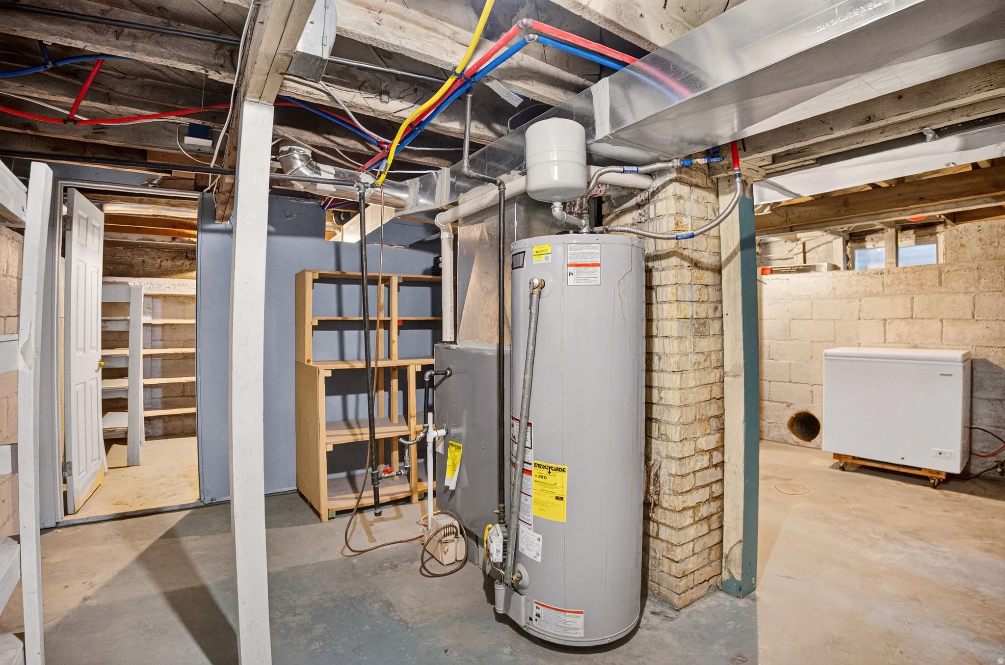 Utility area featuring a water heater, exposed ceiling joists with plumbing, concrete block walls, and concrete flooring