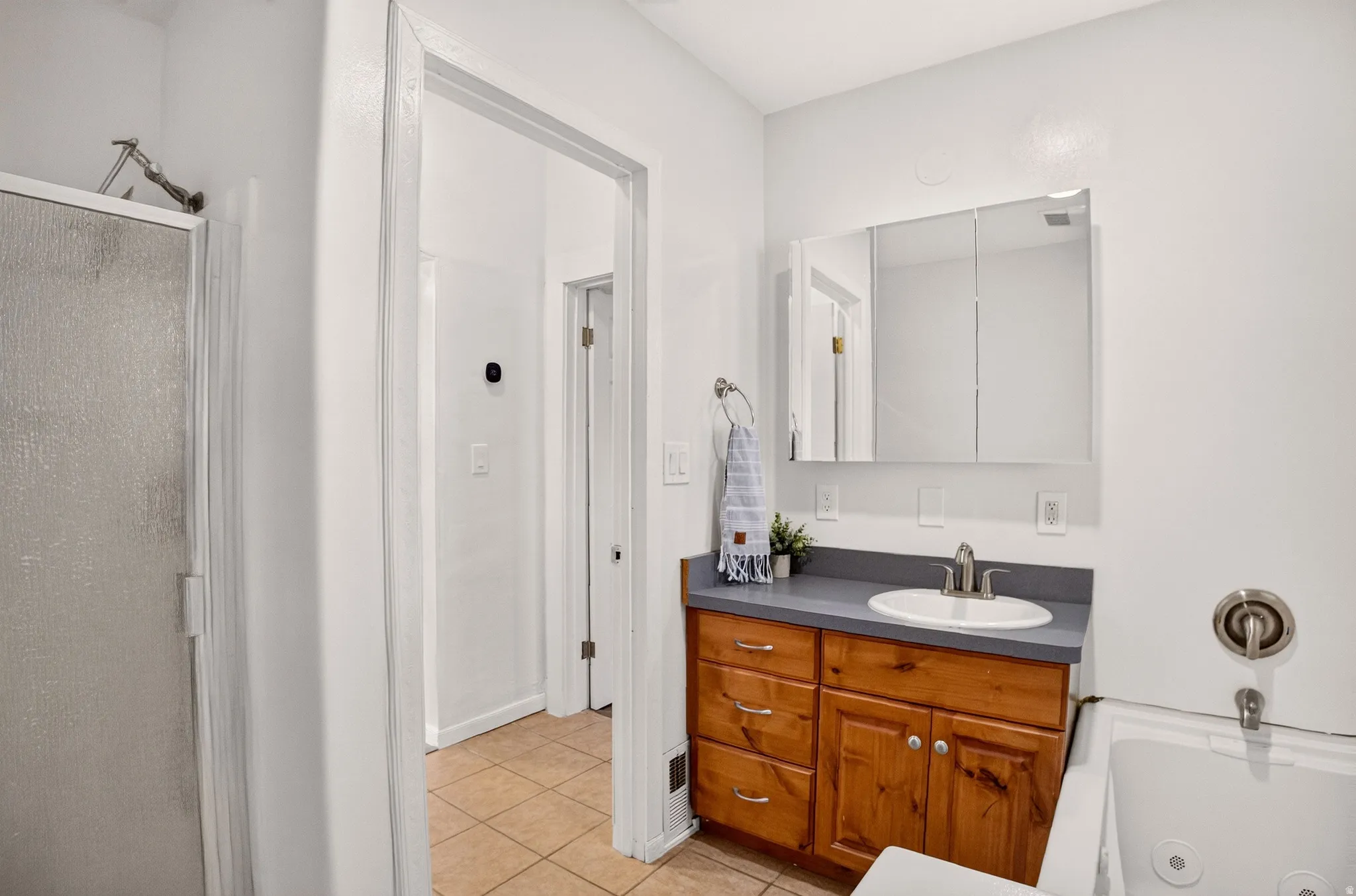 Bathroom featuring a wood vanity with an integrated sink, a medicine cabinet, tile flooring, a glass-enclosed shower, and a built-in tub