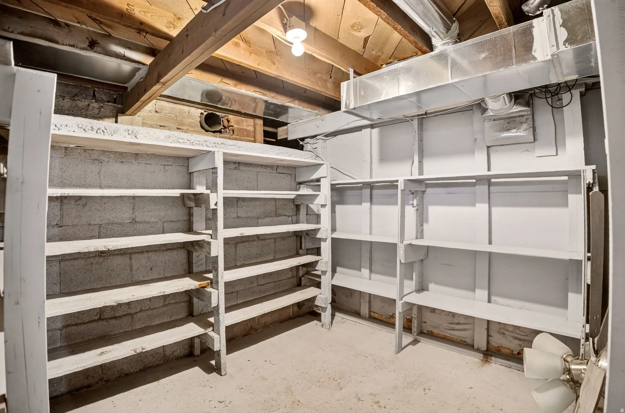 Basement storage area featuring extensive built-in shelving, exposed wood ceiling joists, and concrete block walls