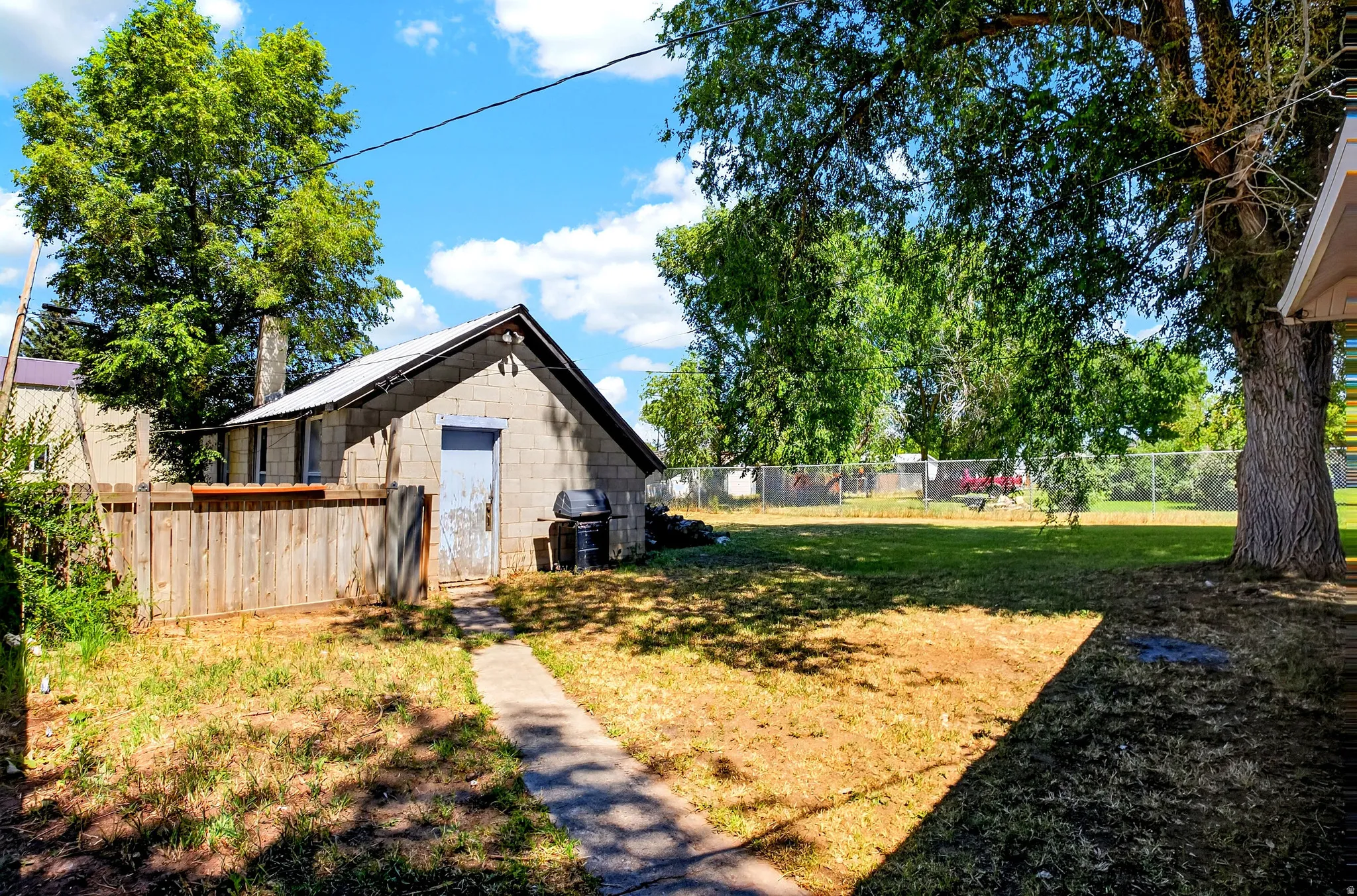 Expansive backyard featuring a concrete block outbuilding with a light blue door, a wood privacy fence, and mature trees