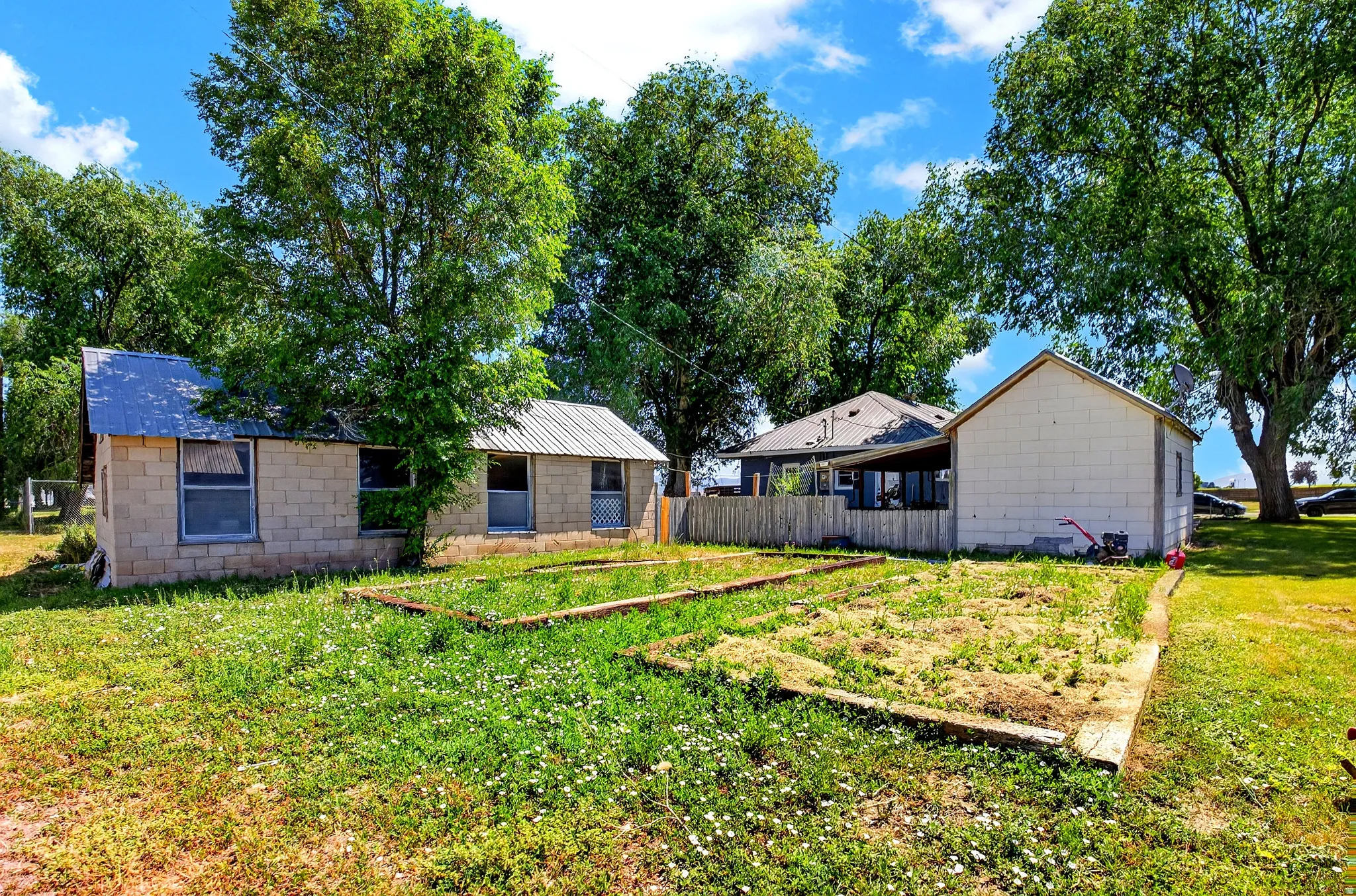 Expansive outdoor space featuring a building with concrete block construction and a metal roof, alongside a second structure with white siding and a covered porch