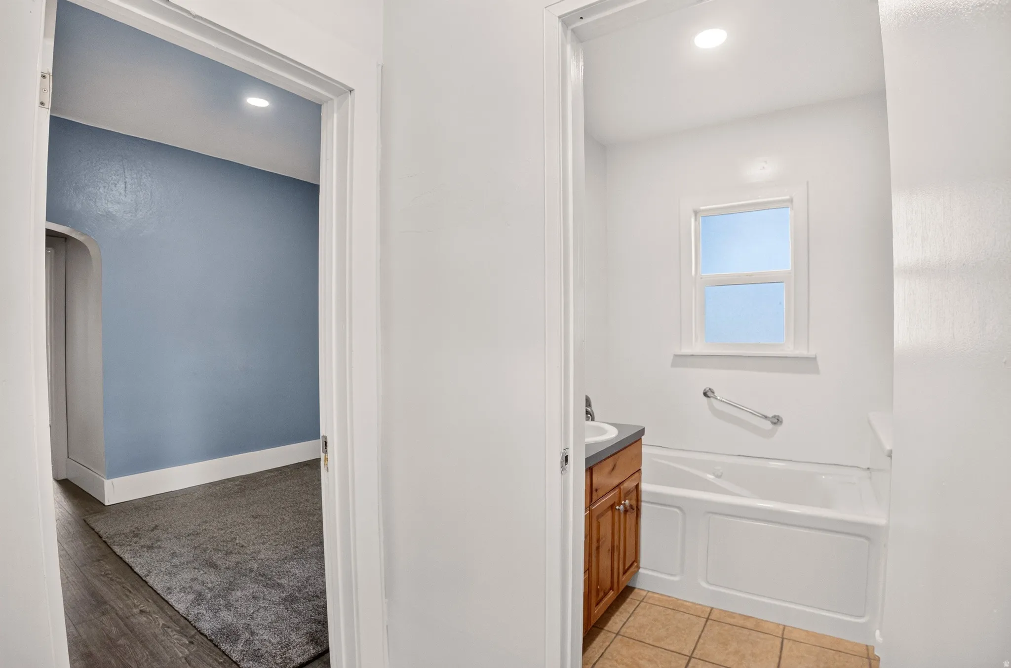 Bathroom featuring a built-in tub, single vanity with a dark countertop, window, and tiled flooring