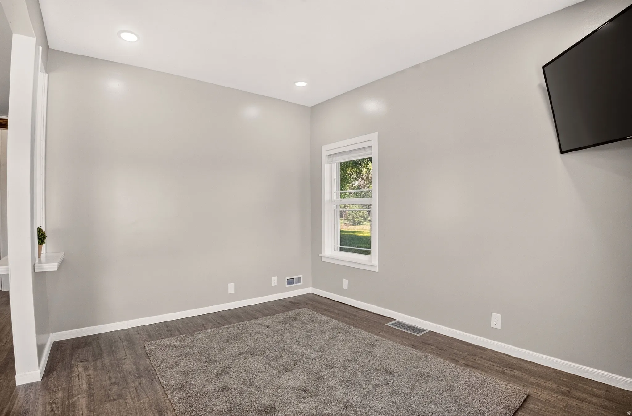 Spacious room with wood-finish flooring, recessed lighting, and a window providing natural illumination