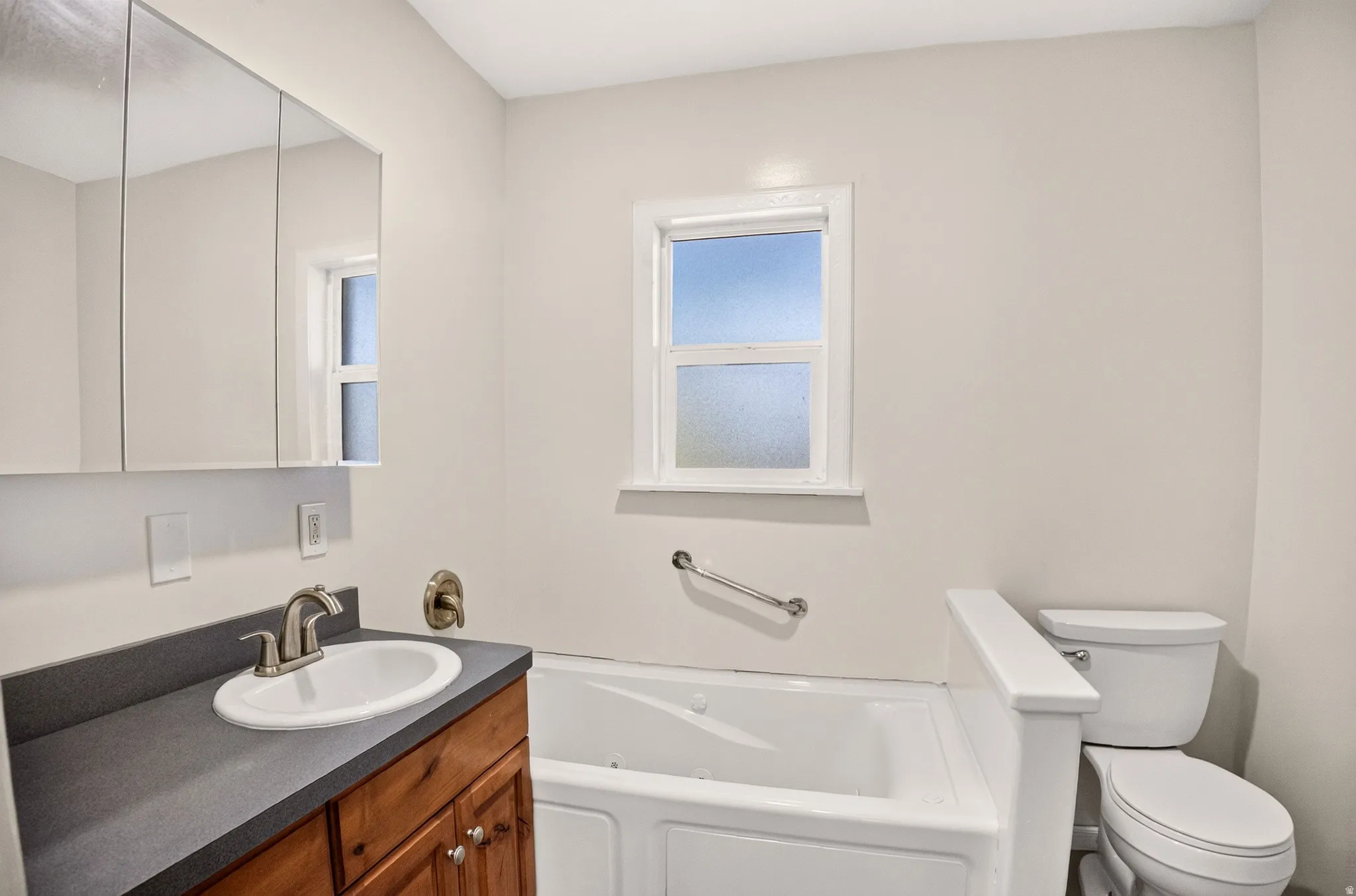 Bathroom featuring a wood vanity with a dark countertop, an undermount sink, and a mirrored medicine cabinet