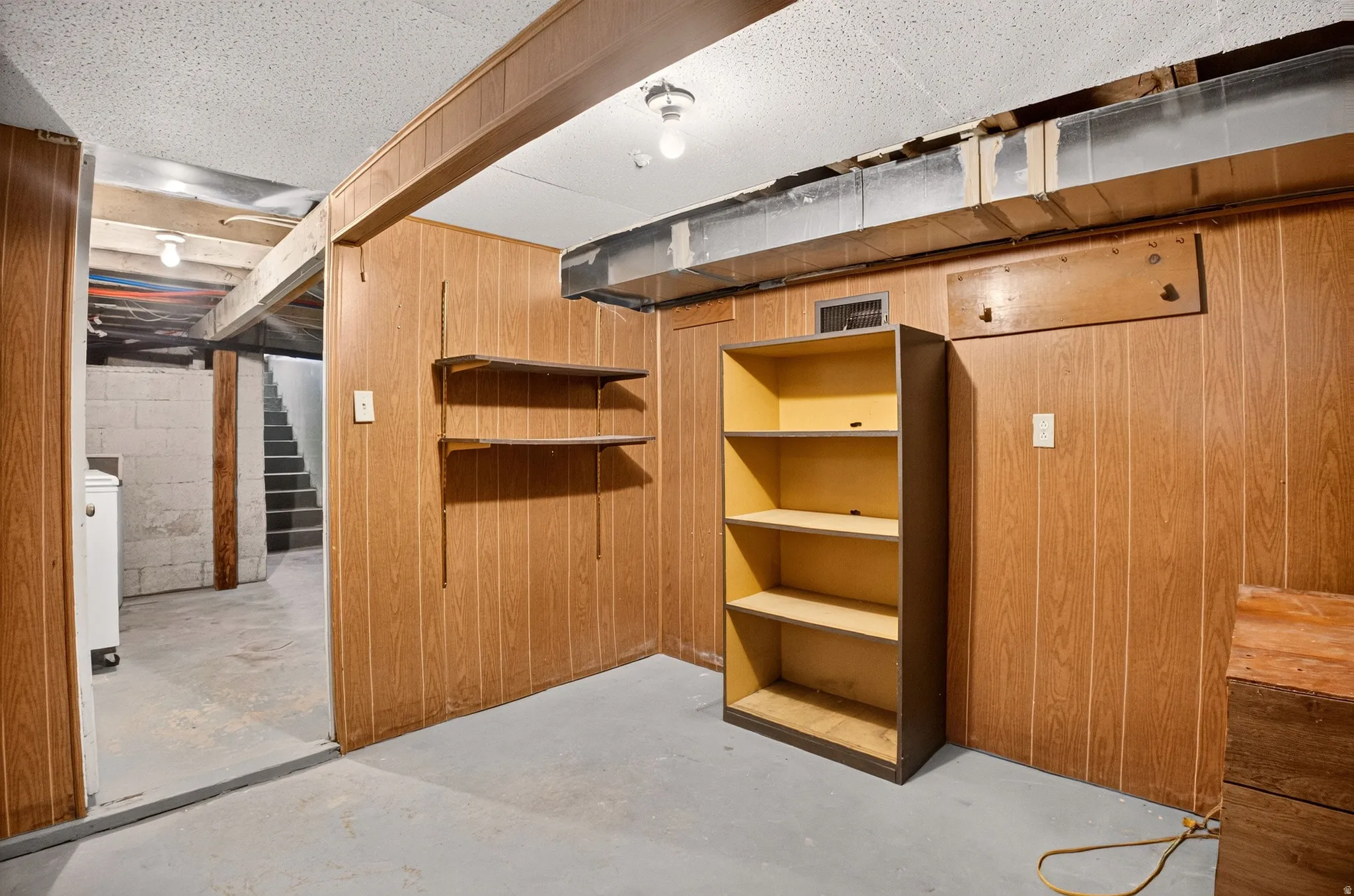 Basement area featuring wood-panel walls, concrete flooring, and exposed ceiling beams