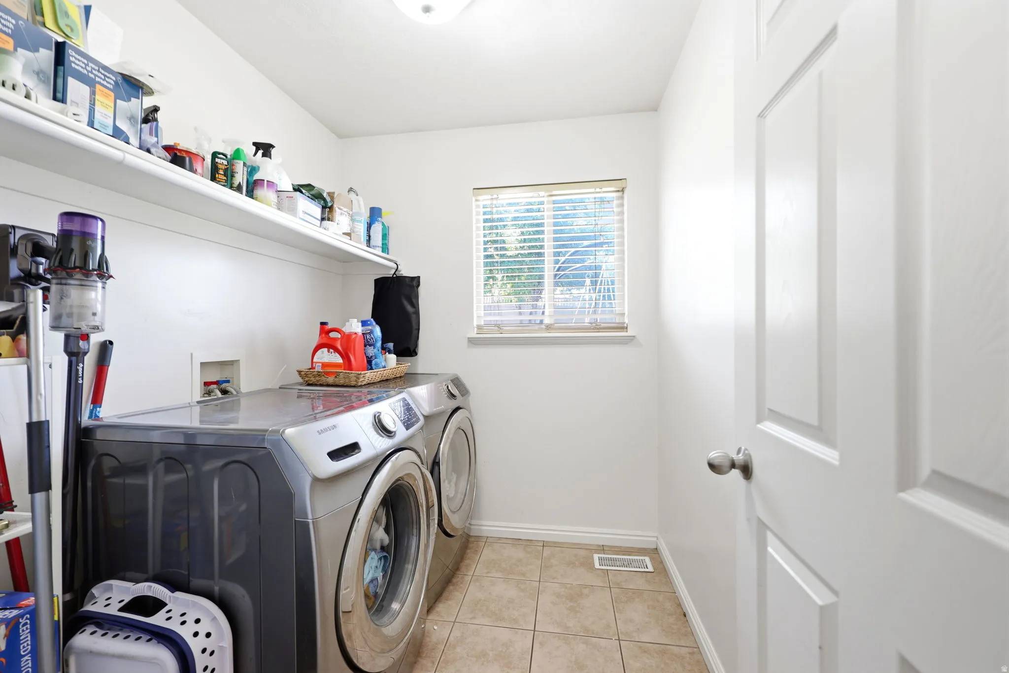 Laundry room featuring tile flooring, a window with blinds, and built-in shelving