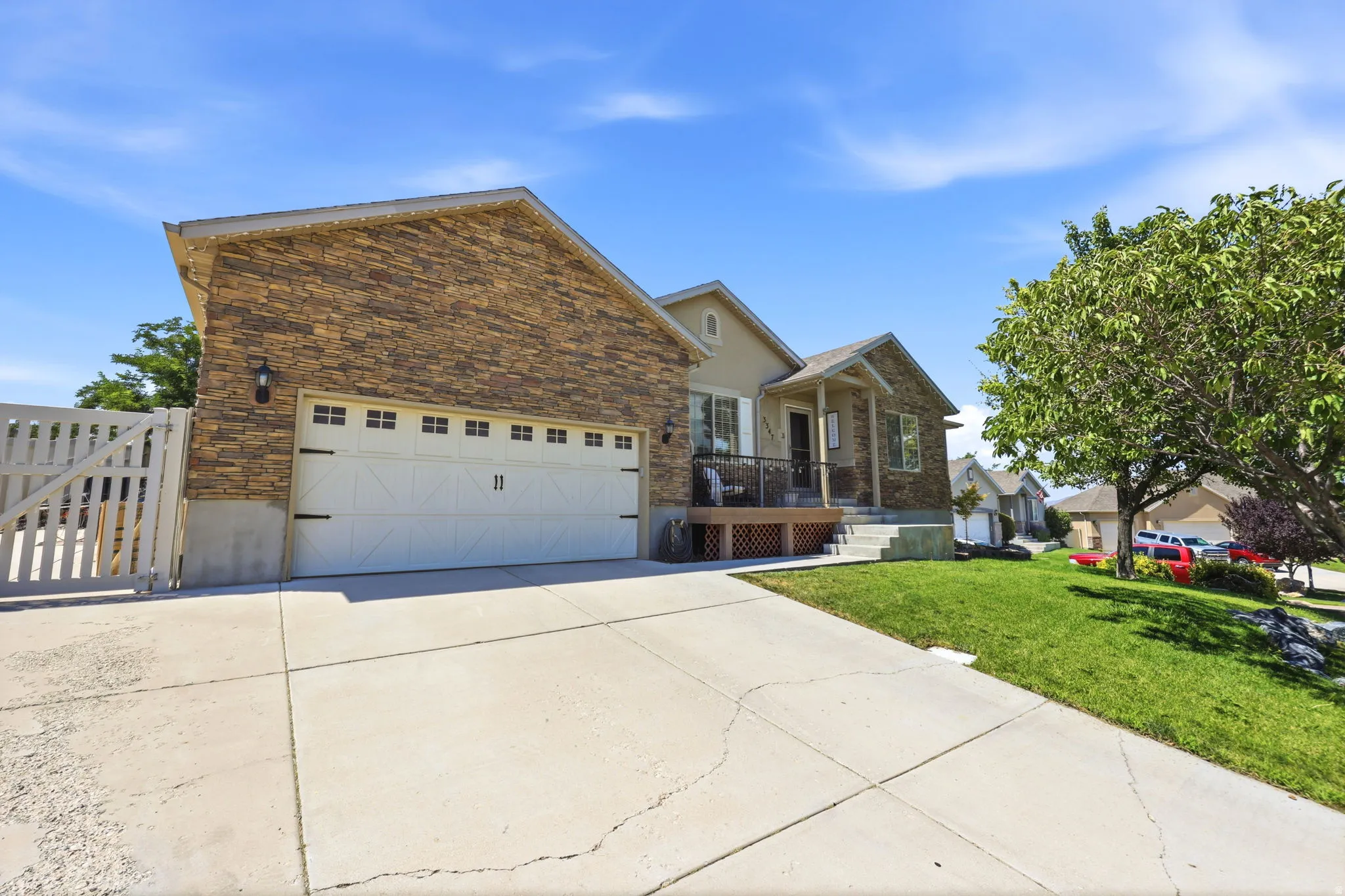 Exterior featuring a stone facade, beige siding, white garage door with decorative hardware, a covered porch, and a concrete driveway