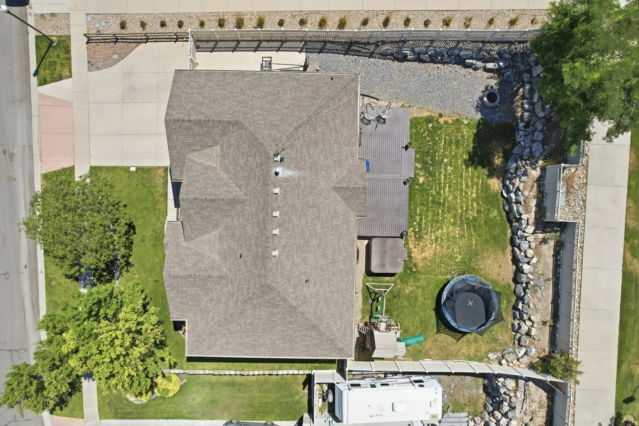 Spacious property featuring a large sloped roof, extensive paved driveway, and a backyard with a deck, lawn, and rock retaining walls