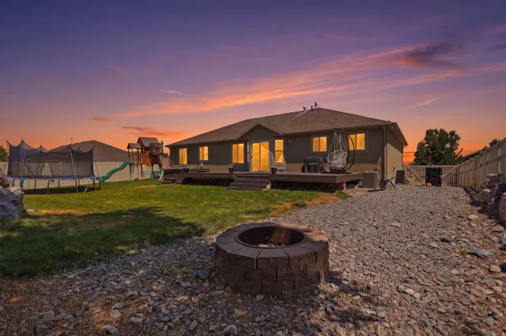 Expansive backyard featuring a built-in fire pit, a gravel path, a wooden deck, and a manicured lawn