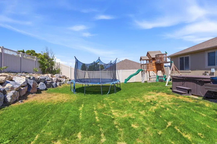 Expansive backyard featuring a large green lawn, a rock retaining wall, a light-colored privacy fence, and a neutral-toned exterior