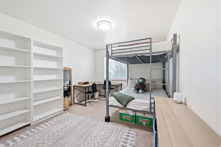 Carpeted room featuring built-in white shelving, a window with blinds, and an overhead flush-mount light fixture