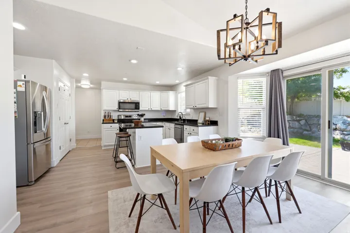 Open concept kitchen and dining area featuring light wood-finish flooring, white cabinetry, dark countertops, and stainless steel appliances