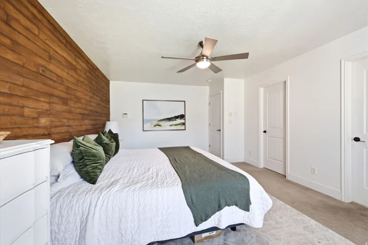 Bedroom featuring a wood accent wall, neutral carpeting, and a ceiling fan with integrated lighting