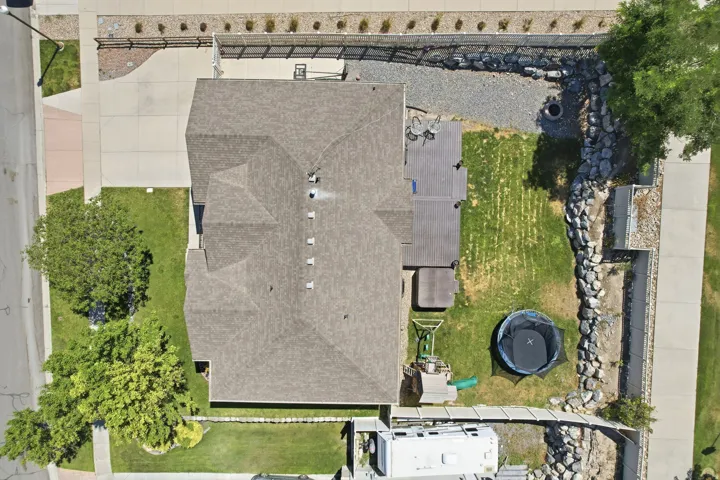 Spacious property featuring a large sloped roof, extensive paved driveway, and a backyard with a deck, lawn, and rock retaining walls