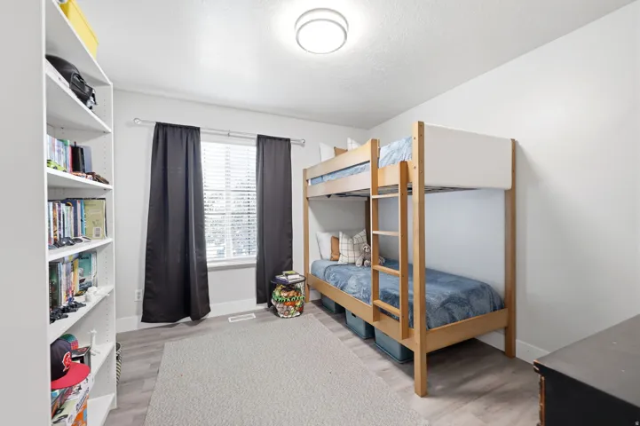 Room featuring light wood-finish flooring, a contemporary ceiling light fixture, and a large window with privacy blinds and dark drapery
