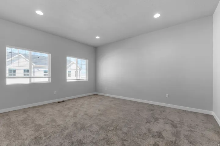 Recessed lighting, light gray walls, two windows with blinds, and neutral carpeting
