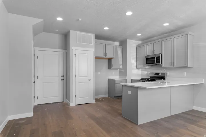 Open-concept kitchen featuring an island, light gray cabinetry, stainless steel appliances, and wood-finish flooring