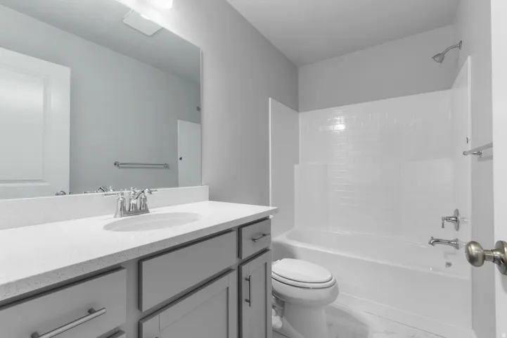 Bathroom featuring a white integrated sink, gray cabinetry, speckled white countertop, and a white subway tile tub surround