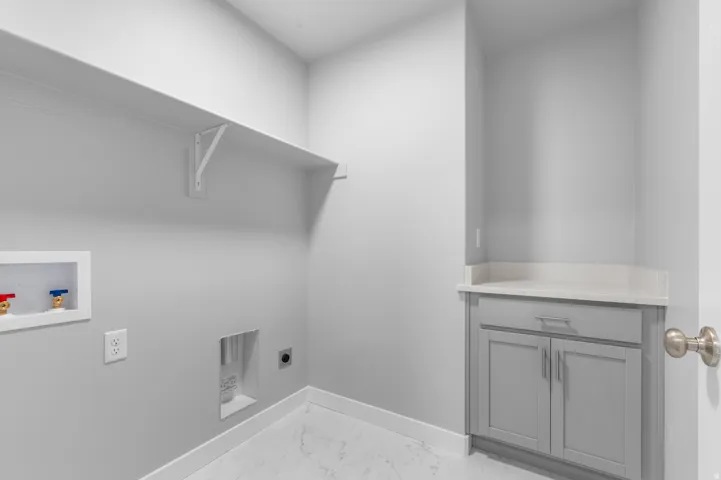 Laundry area featuring a built-in shelf, modern cabinetry with a light-toned countertop, and white tile flooring