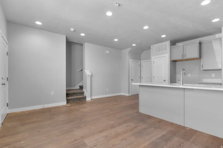 Wood-finish flooring, recessed lighting, light gray cabinetry, white countertops, and a stainless steel gooseneck faucet