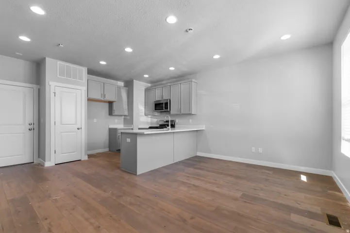 Open-concept living space featuring wood-finish flooring, recessed lighting, and a kitchen with gray cabinetry, white countertops, and stainless steel appliances