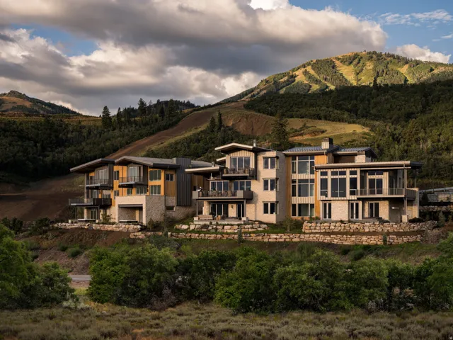 Modern mountain residences featuring extensive window arrays, multiple balconies, stone veneer accents, wood-finish siding, and integrated retaining walls