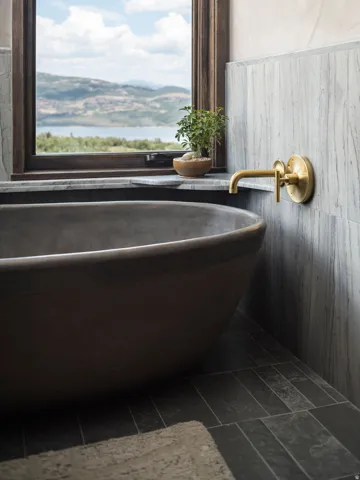 Freestanding soaking tub set against a window with a mountain and lake backdrop