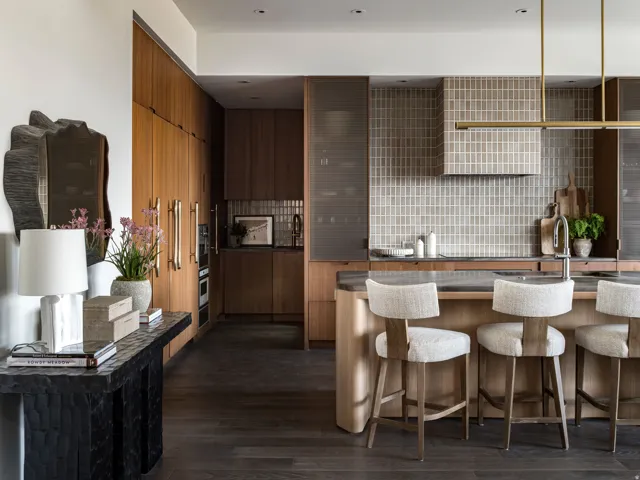 Gourmet kitchen featuring a waterfall island, integrated appliances, wood-finish cabinetry, and a full-height tiled backsplash