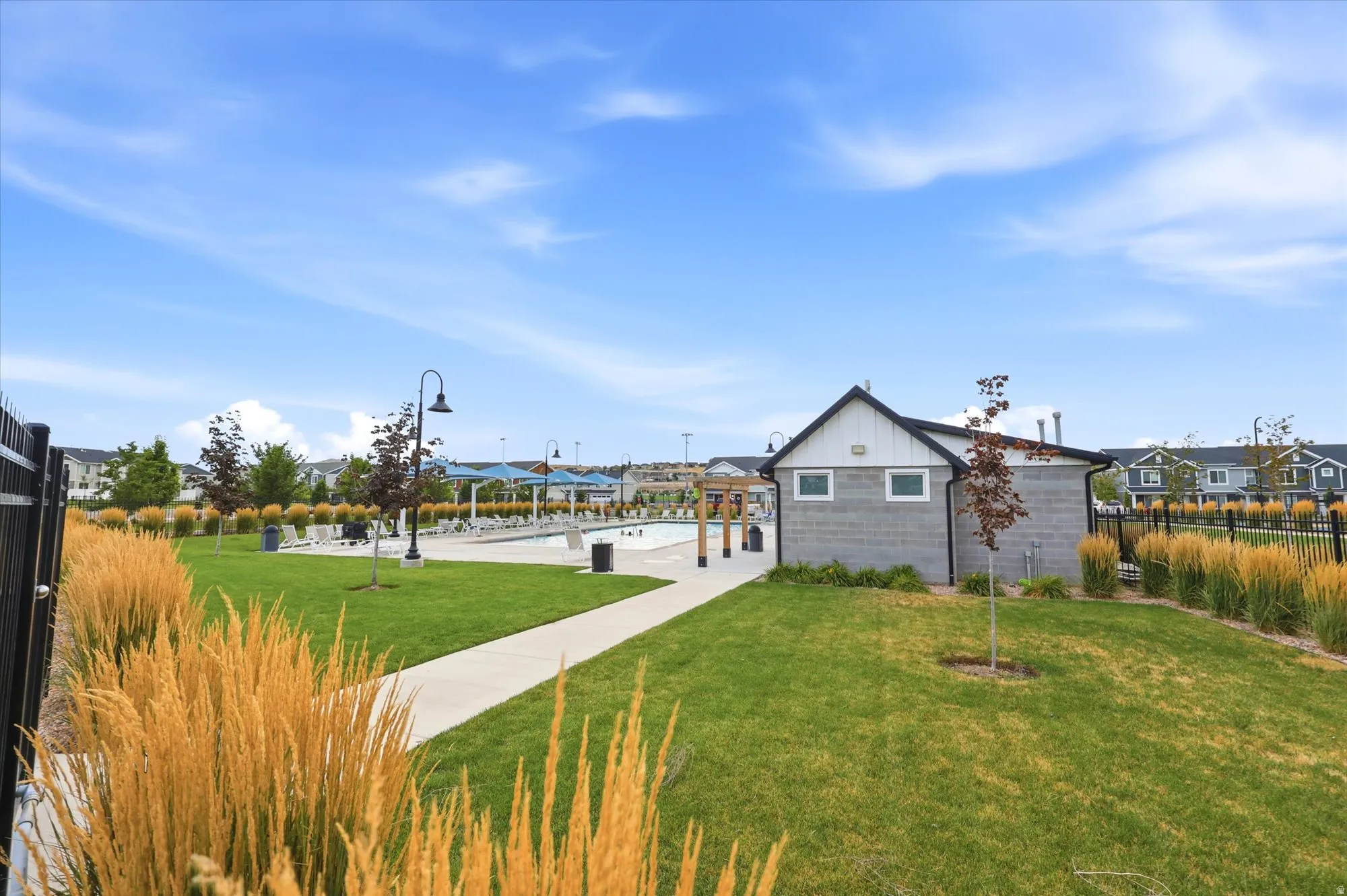 Community amenity space featuring a swimming pool, shaded lounge areas, and a modern pool house