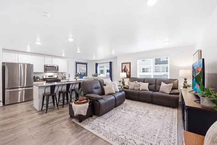 Open-concept living space featuring wood-finish flooring, a kitchen island with seating, stainless steel appliances, white cabinetry, and recessed lighting