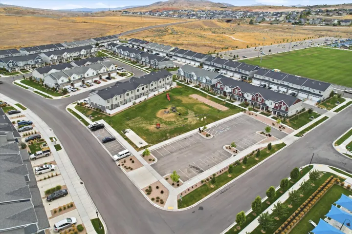 Community green space with playground equipment, surrounded by residential townhomes featuring multi-tone exteriors, paved streets, and organized parking areas
