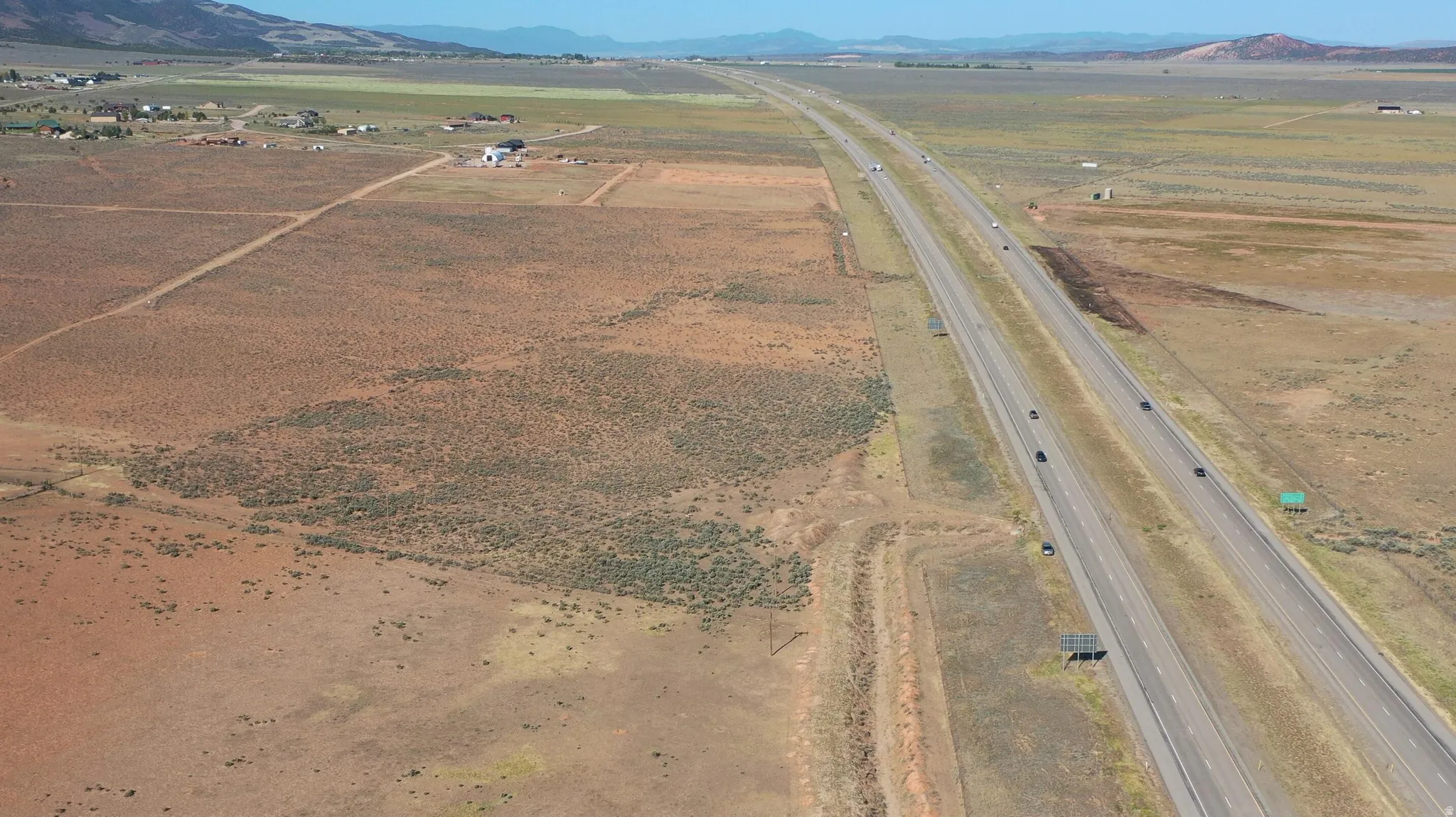 Expansive rural land parcel featuring a visible highway, distant mountains, and scattered brush