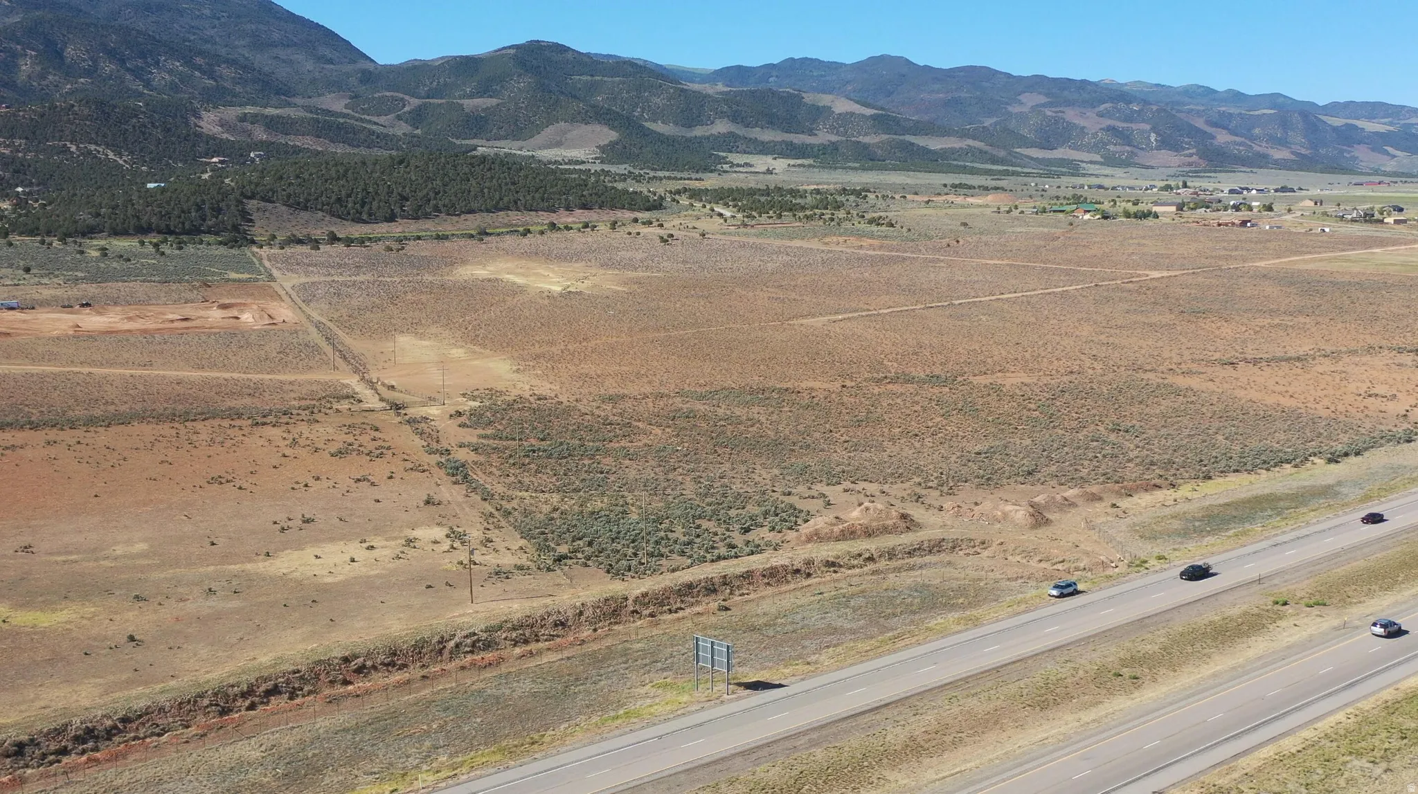 Expansive undeveloped land featuring natural desert vegetation, a visible highway frontage, and distant mountain backdrops