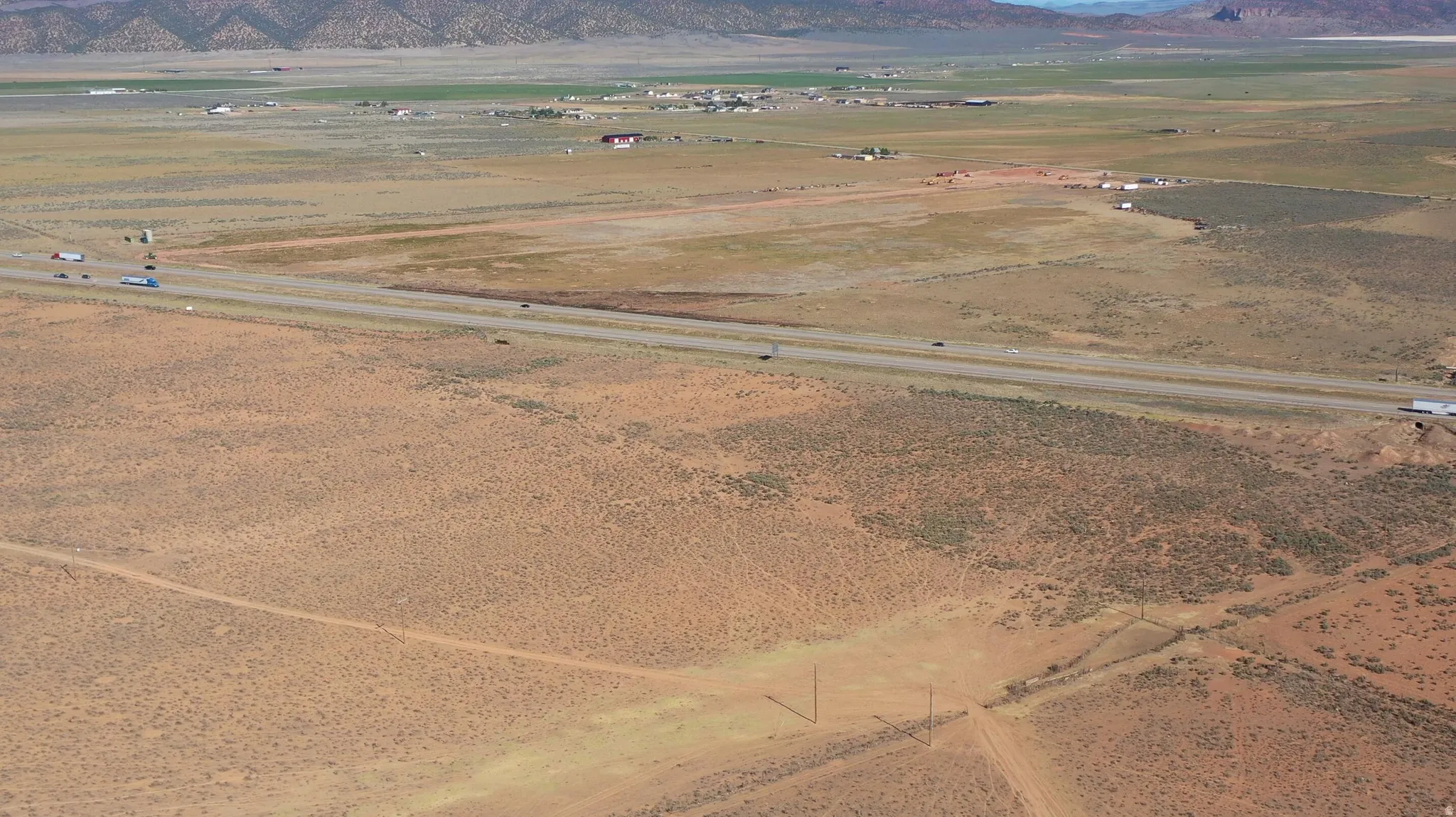 Expansive desert landscape featuring a multi-lane highway, distant mountains, and scattered brush