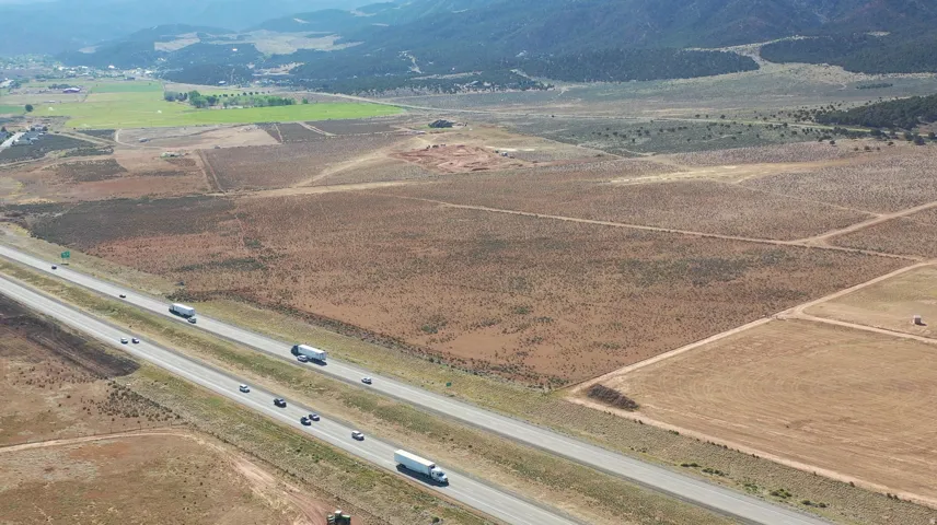 Expansive open land featuring a prominent highway, distant green fields, and mountainous terrain in the background