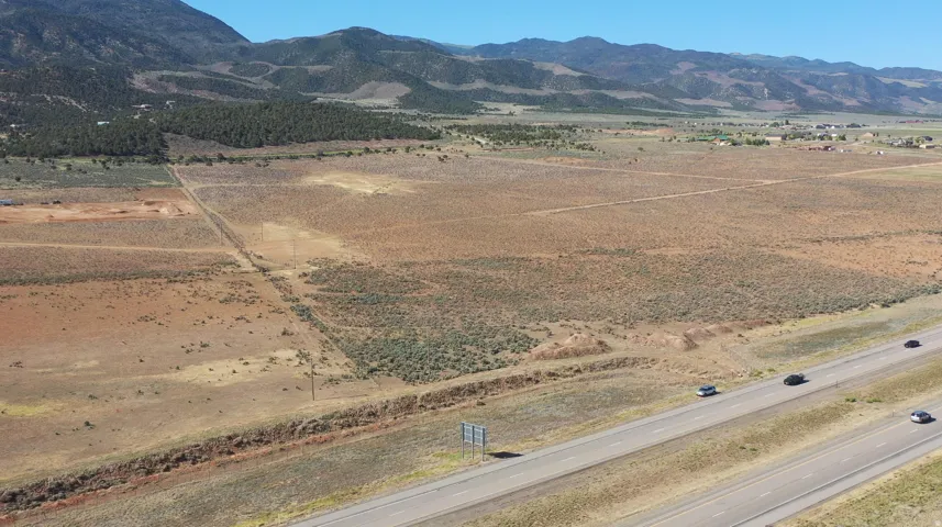 Expansive undeveloped land featuring natural desert vegetation, a visible highway frontage, and distant mountain backdrops