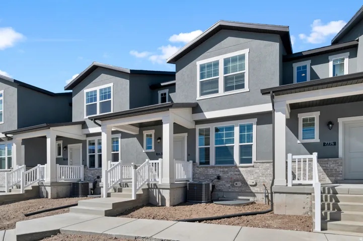 Contemporary townhouse exterior featuring a gray stucco finish, white trim, stone accents, and covered entryways with white railings