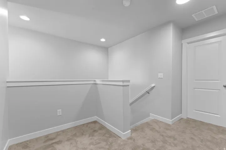 Recessed lighting, light gray wall paint, white trim, light gray carpeting, and a white two-panel door