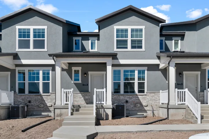 Contemporary townhouse facade featuring stucco siding, white-framed windows, and a brick accent foundation
