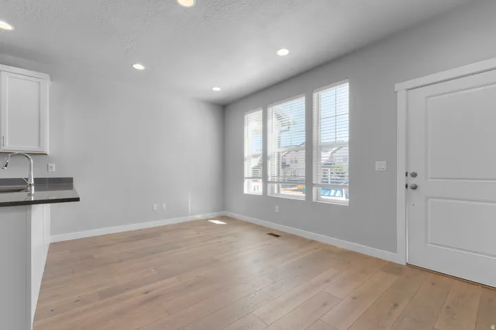 Recessed lighting, wood-finish flooring, white paneled door, kitchen counter with sink, and three vertical windows