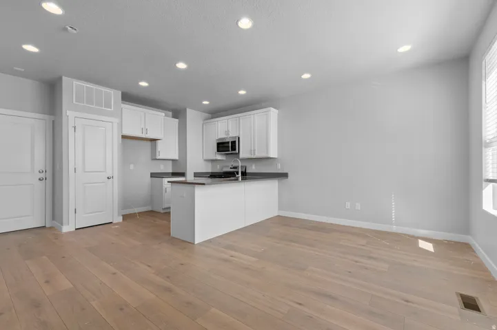 Recessed lighting illuminates the open-concept layout, featuring wood-finish flooring and a kitchen island with dark countertops