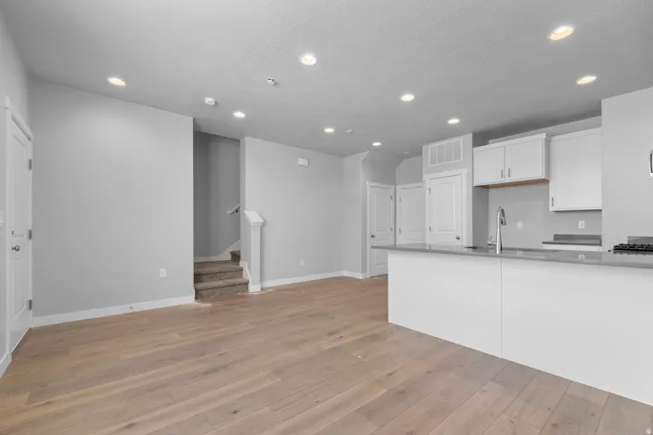 Wood-finish flooring throughout, recessed ceiling lighting, kitchen island with counter seating, white cabinetry, and stainless steel kitchen faucet