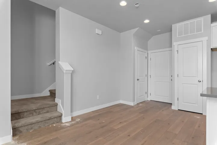 Light wood-finish flooring, recessed ceiling lighting, gray wall paint, white trim, and a carpeted staircase