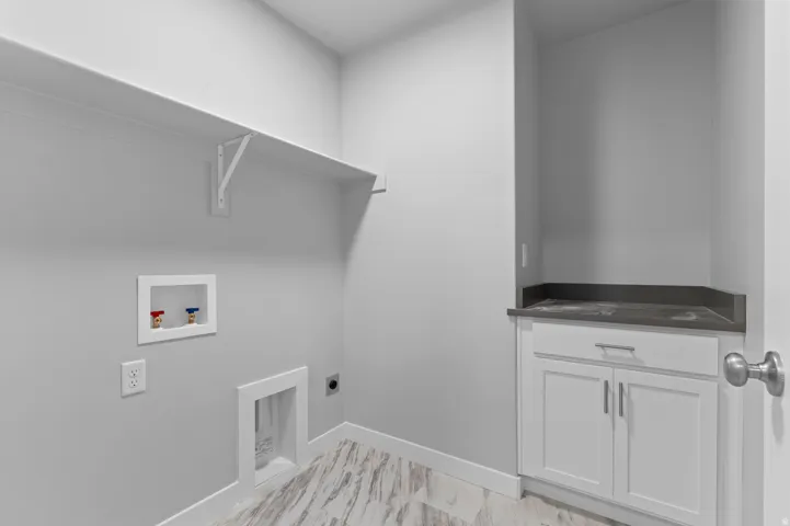 Laundry area with wood-finish flooring, built-in shelving, white cabinetry, and dark countertop