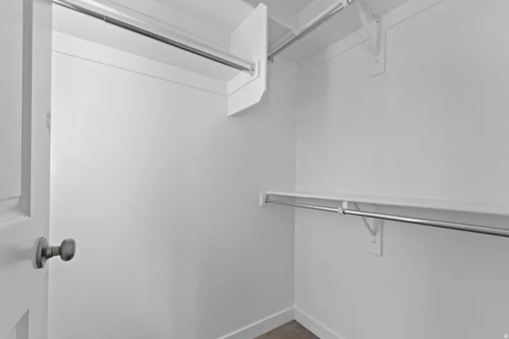 Walk-in closet featuring white walls, shelving, and chrome hanging rods