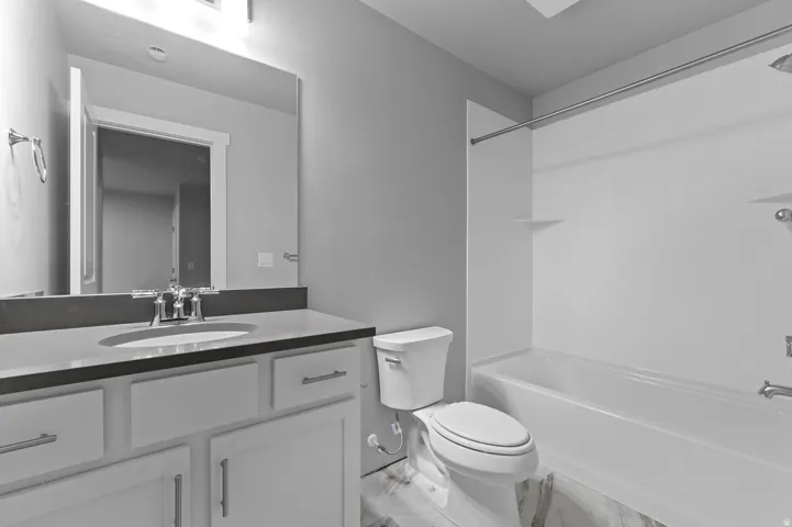 Bathroom featuring an integrated bathtub and shower, a single vanity with an undermount sink, a large wall-mounted mirror, and tile flooring