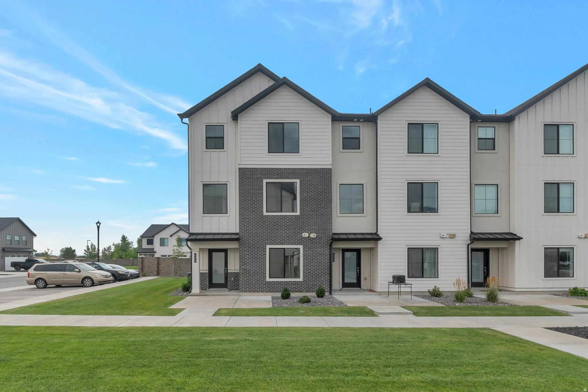 Modern townhome exterior featuring vertical and horizontal siding, dark brick accents, a dark-colored roof, and multiple large windows