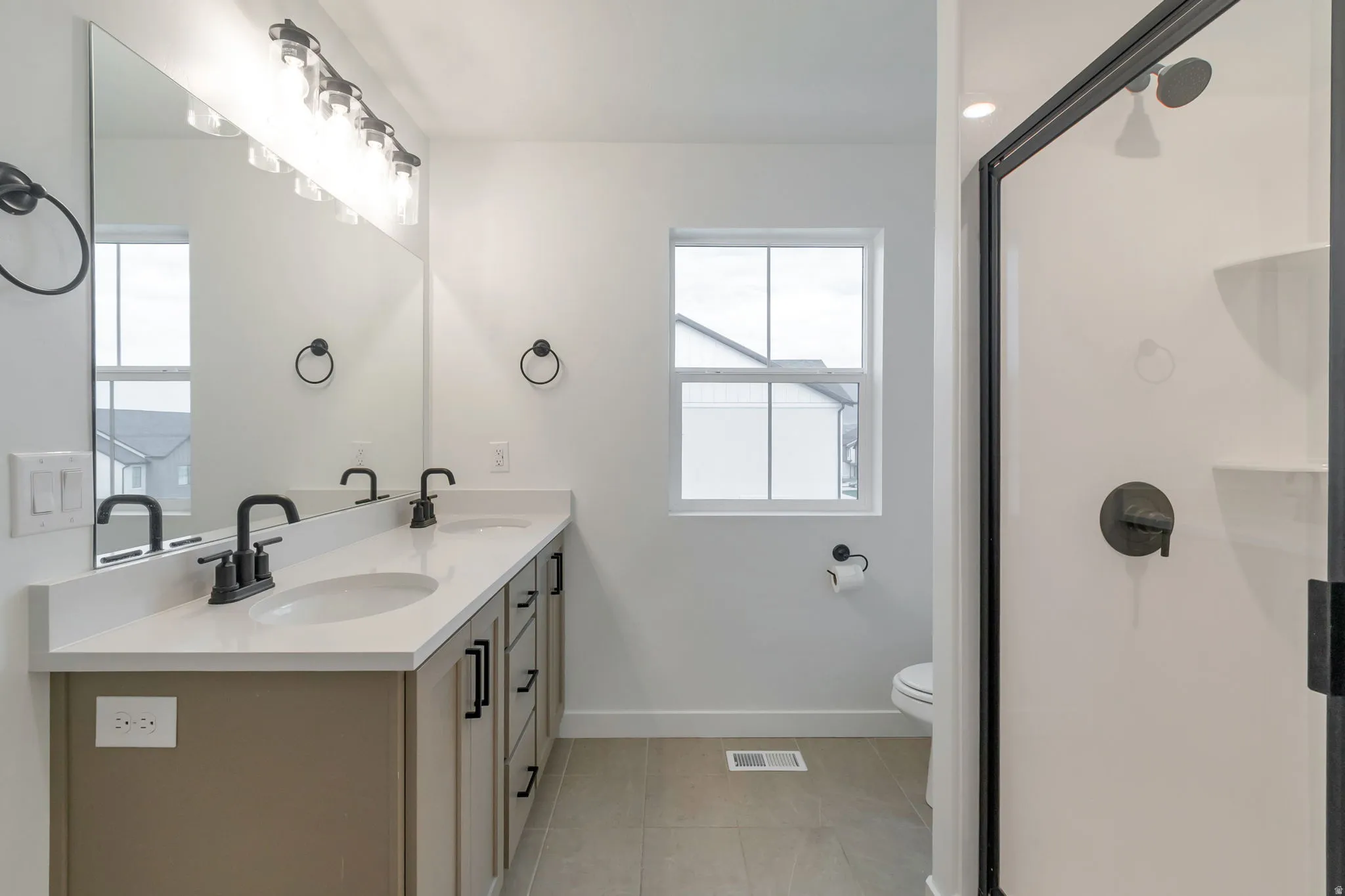 Bathroom featuring a dual vanity with light-toned cabinetry, light countertop, and matte black fixtures